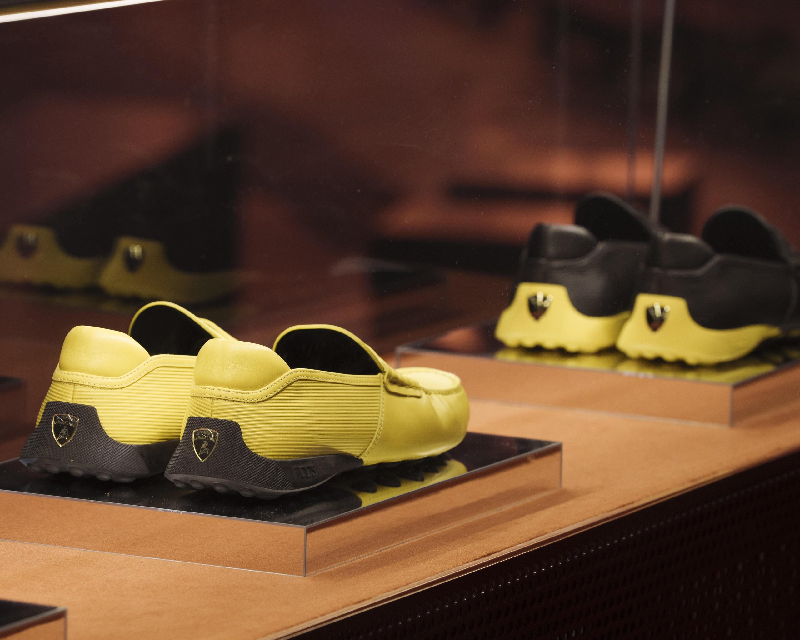 Tod'S X Automobili Lamborghini: What A Driving Shoe Tells You About Where The Brand Is Headed 9 Rear view of yellow and black tod's for automobili lamborghini driving shoes on a shelf showing the lamborghini shield logo on the heel