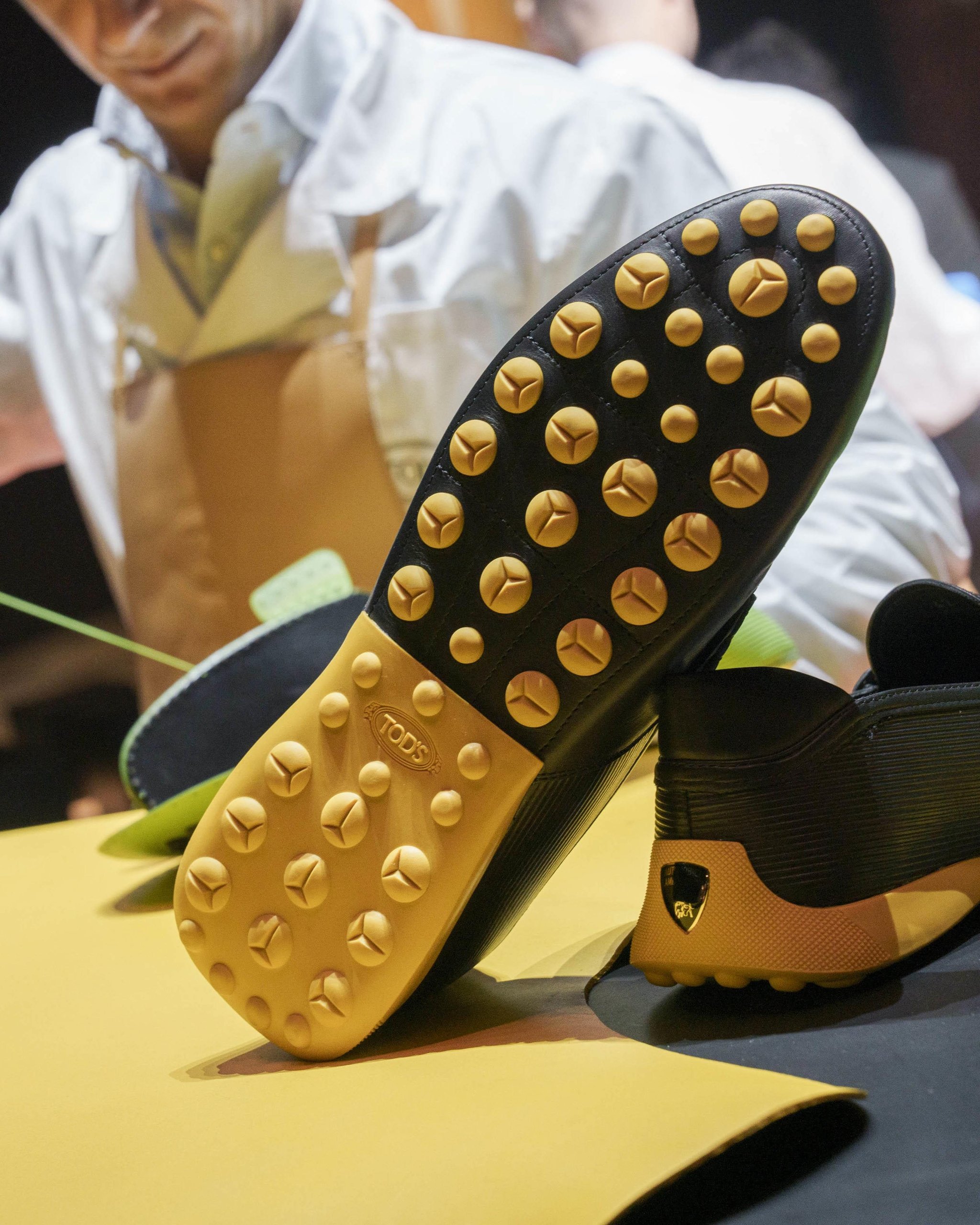 Tod'S X Automobili Lamborghini: What A Driving Shoe Tells You About Where The Brand Is Headed 11 Close-up of a black tod's for automobili lamborghini driving shoe sole featuring yellow rubber pebbles and the tod's logo with a craftsman blurred in the background