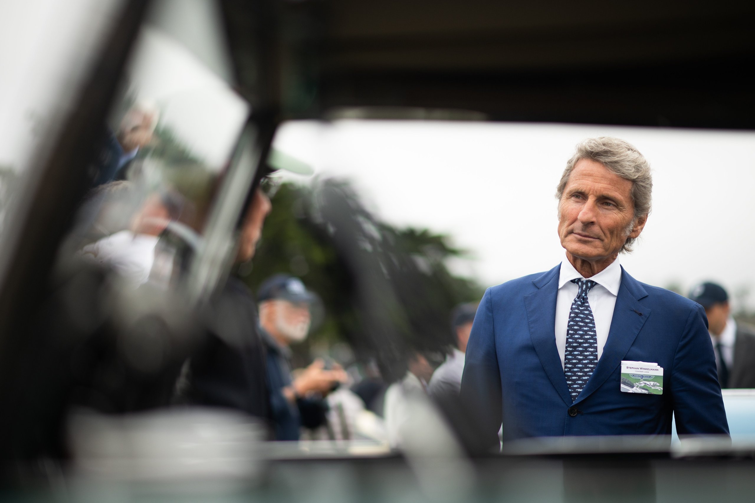 Lamborghini Brought A Mountain Record To The Most Exclusive Lawn In America 9 A man in a blue suit and patterned tie wearing an event badge at the pebble beach concours d'elegance