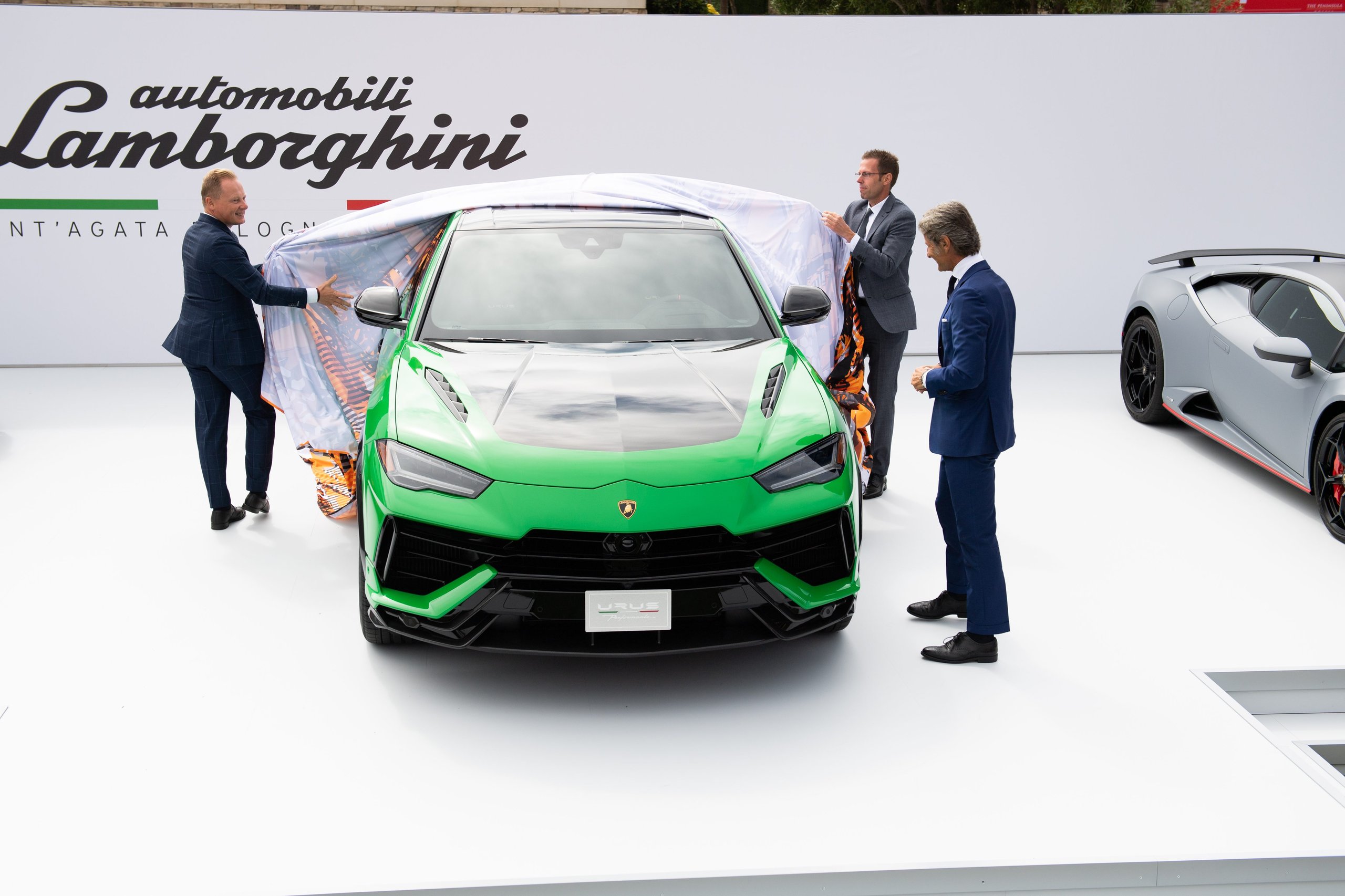 How Lamborghini Turned The Quail Into A Heritage Argument For The Urus Performante 3 Two men unveil the green lamborghini urus performante on a white stage at the quail, with the fabric cover being pulled away