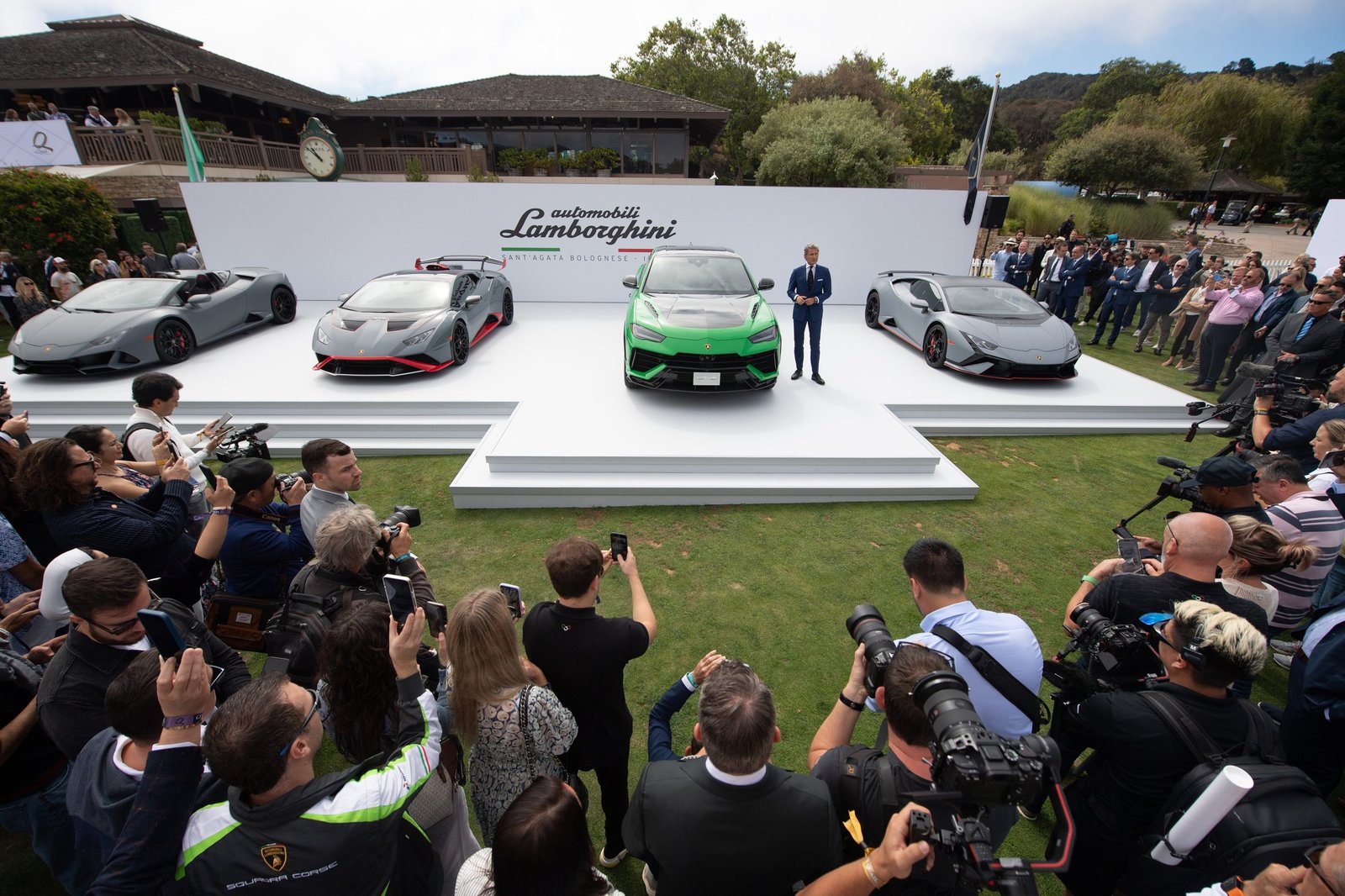 Stephan Winkelmann presents the green Lamborghini Urus Performante on stage at The Quail, flanked by Huracán models and a large crowd