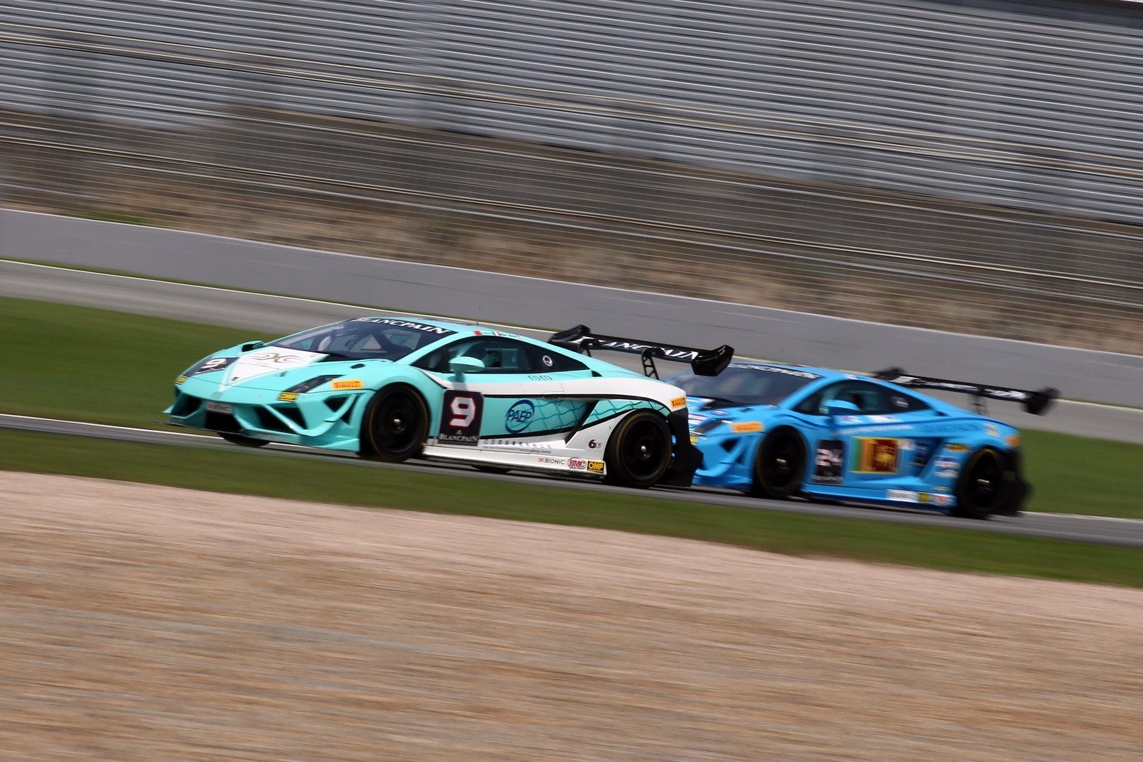 Two blue Lamborghini Gallardo Super Trofeo race cars in close competition on track, showing aerodynamic body kits, large rear wings, and racing liveries