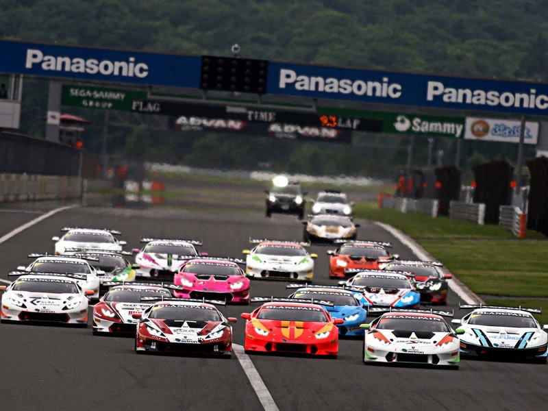 A pack of multi-colored Lamborghini Huracán GT3 race cars battling for position on a wet racetrack during the Blancpain Super Trofeo series