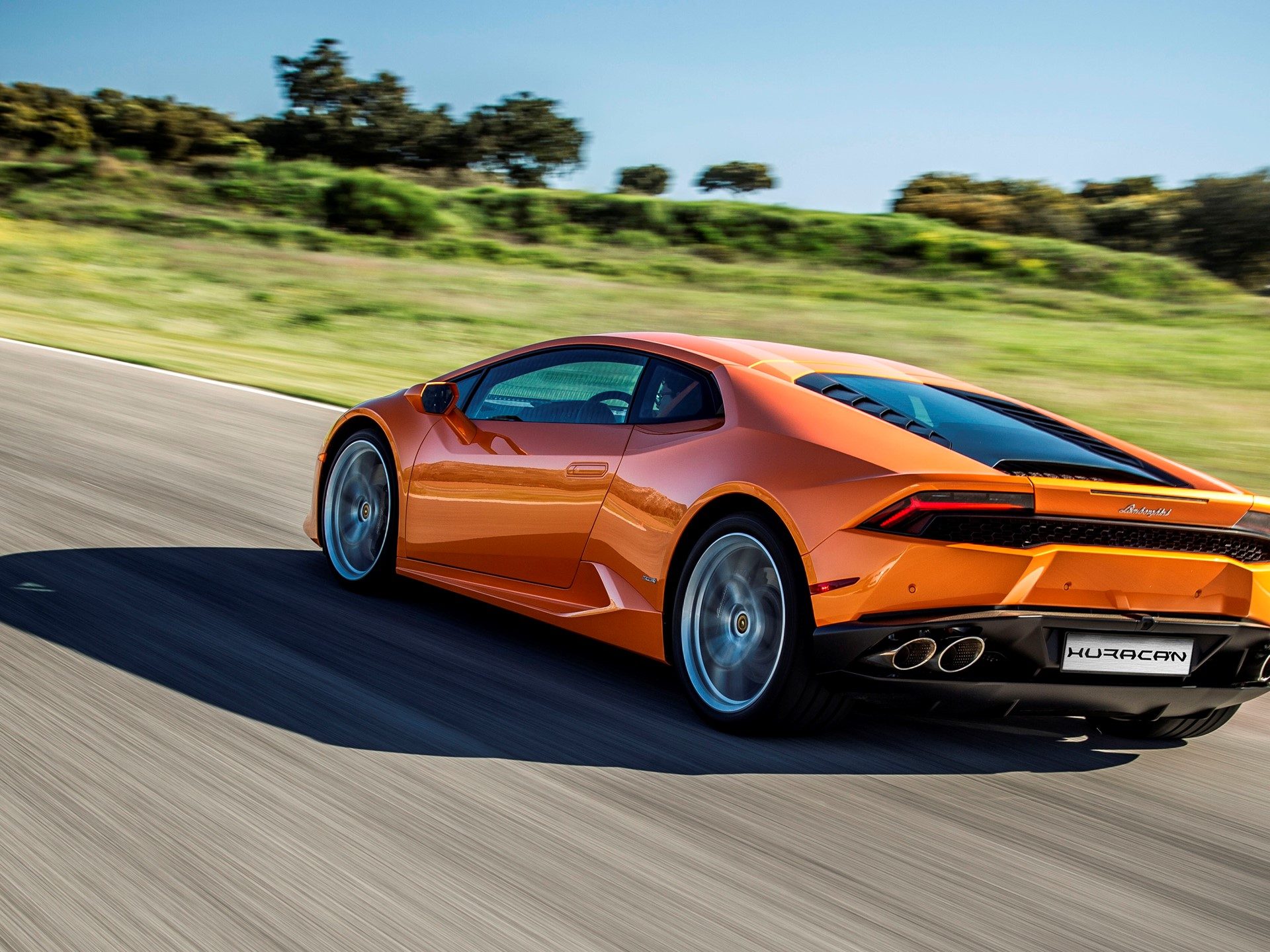 Orange Lamborghini Huracán LP 610-4 at speed on a racetrack, rear three-quarter view showing the aggressive diffuser and dual exhaust tips