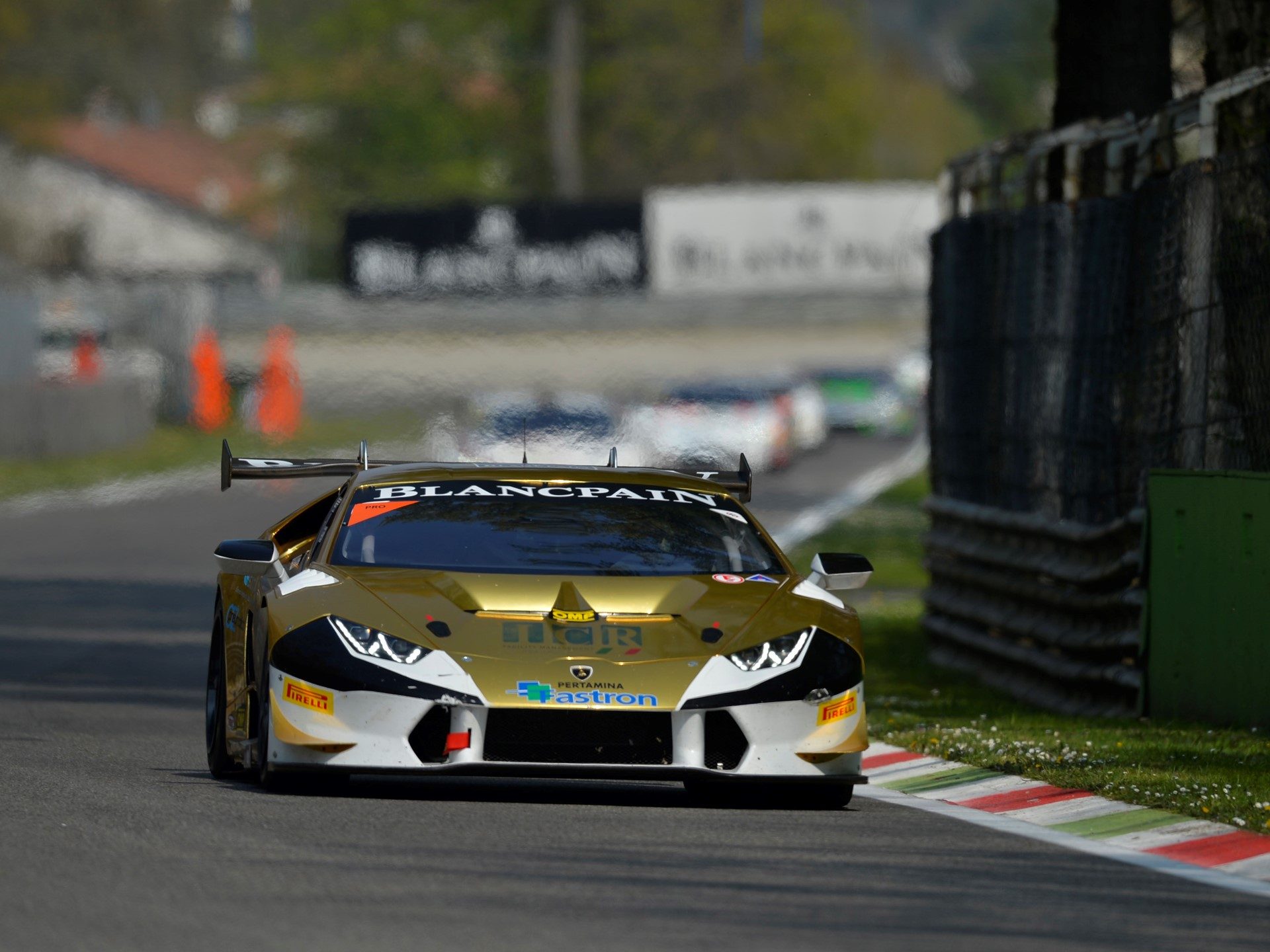 Gold and white Lamborghini Huracán LP 620-2 Super Trofeo racing at speed on track with competitors in the background