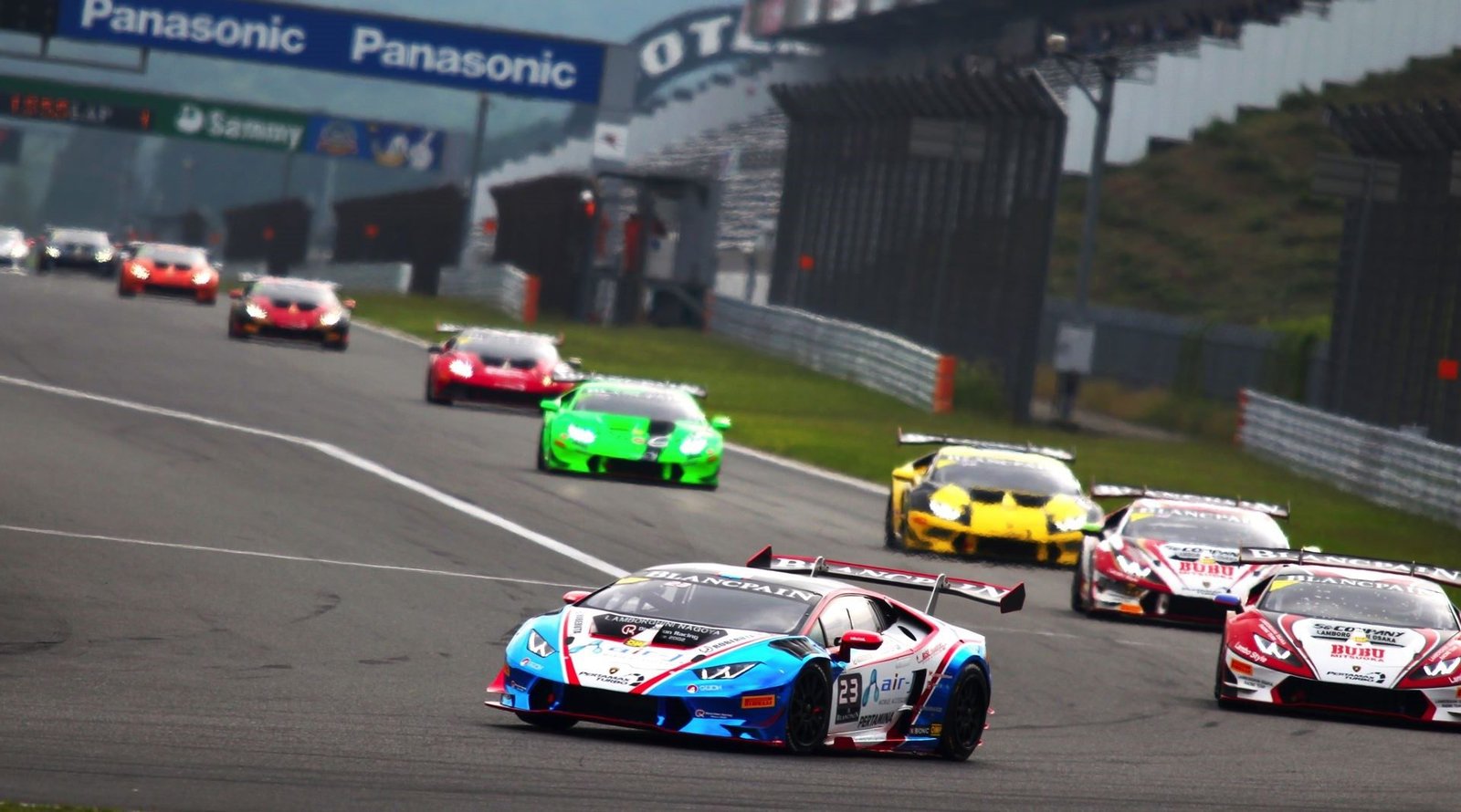 A multi-colored Lamborghini Huracán race car leads a pack of competitors on the Fuji International Speedway circuit during the 2016 Blancpain Super Trofeo Asia series