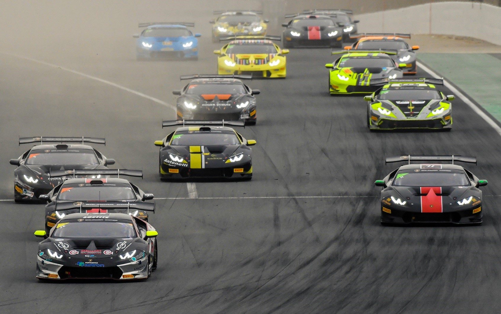 A pack of Lamborghini Huracán Super Trofeo race cars in varied liveries battle for position on track during the Super Trofeo Asia series