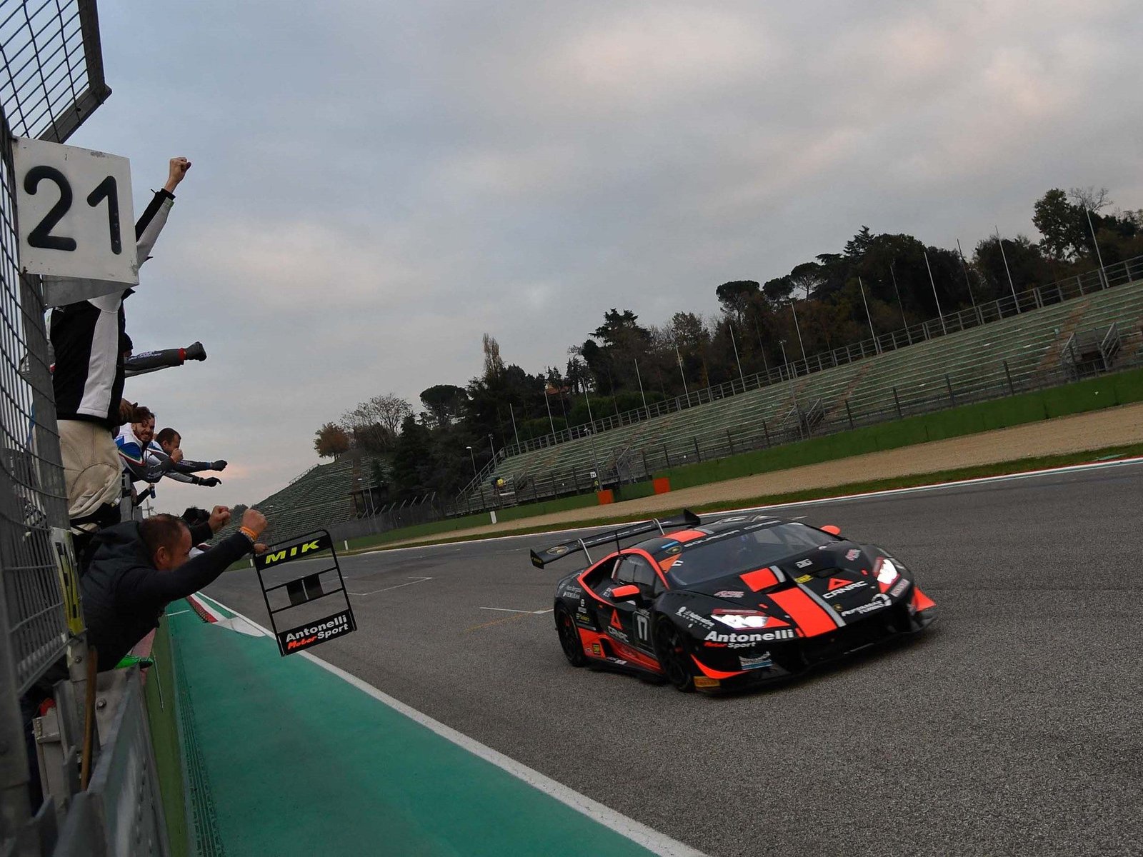 A black and orange Lamborghini Huracán Super Trofeo race car speeds past cheering spectators at Imola during the 2017 season finale