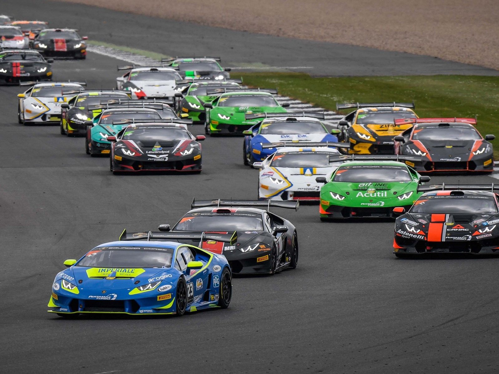 Multiple Lamborghini Huracán Super Trofeo race cars in various liveries battling for position on a racetrack