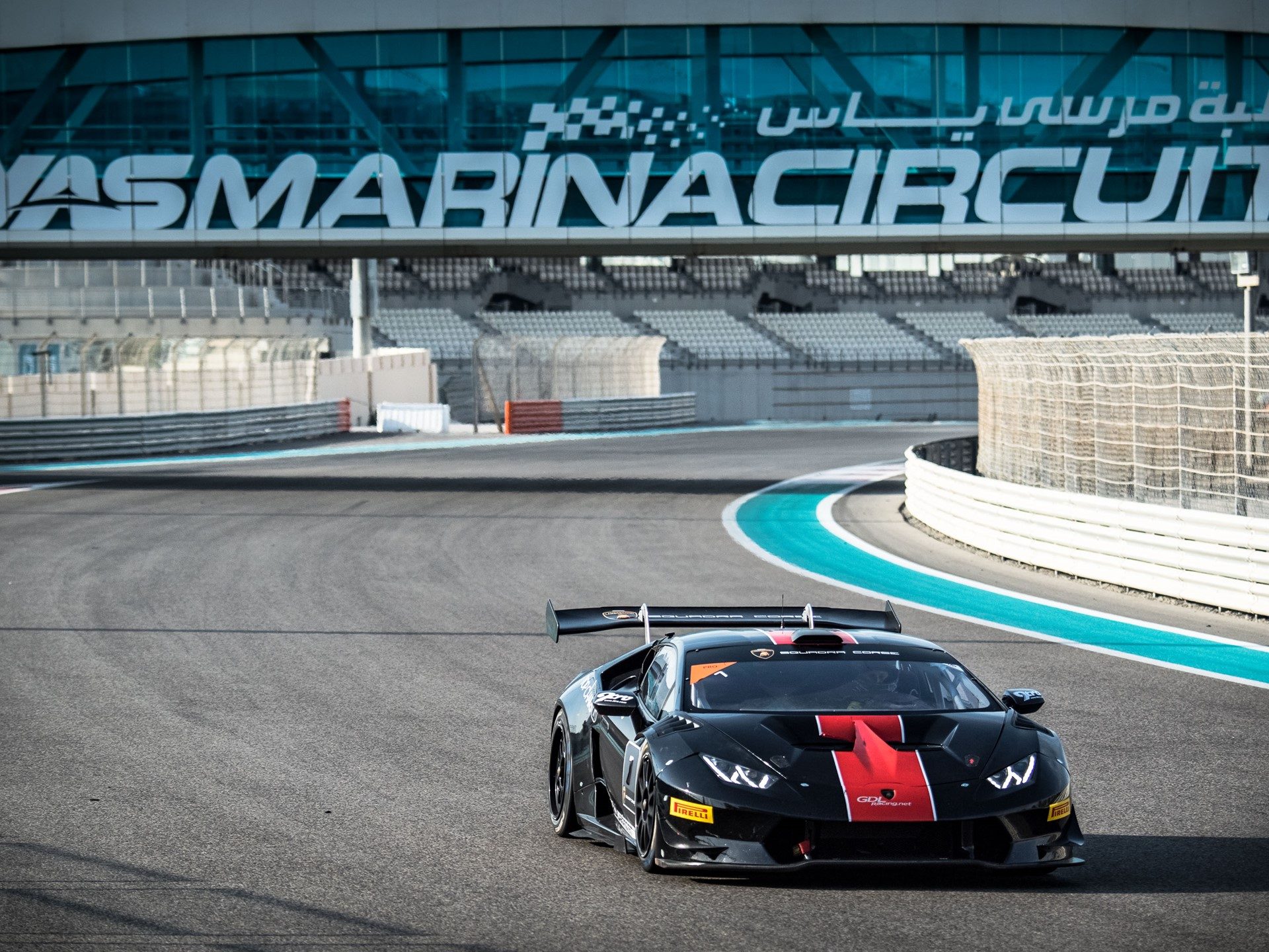 Black Lamborghini Huracán Super Trofeo with red accents racing on the Yas Marina Circuit with grandstands in the background