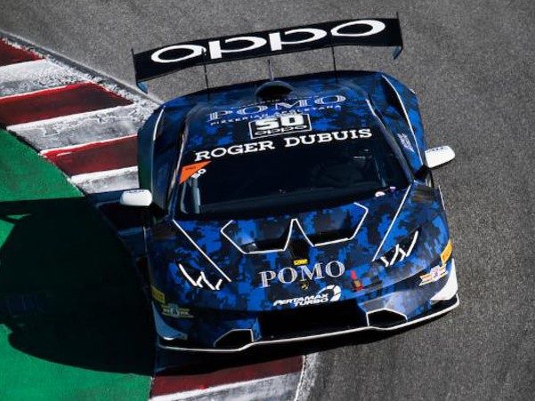 Blue camouflage-liveried Lamborghini Huracán Super Trofeo race car on track at speed, showing aggressive aero and large rear wing