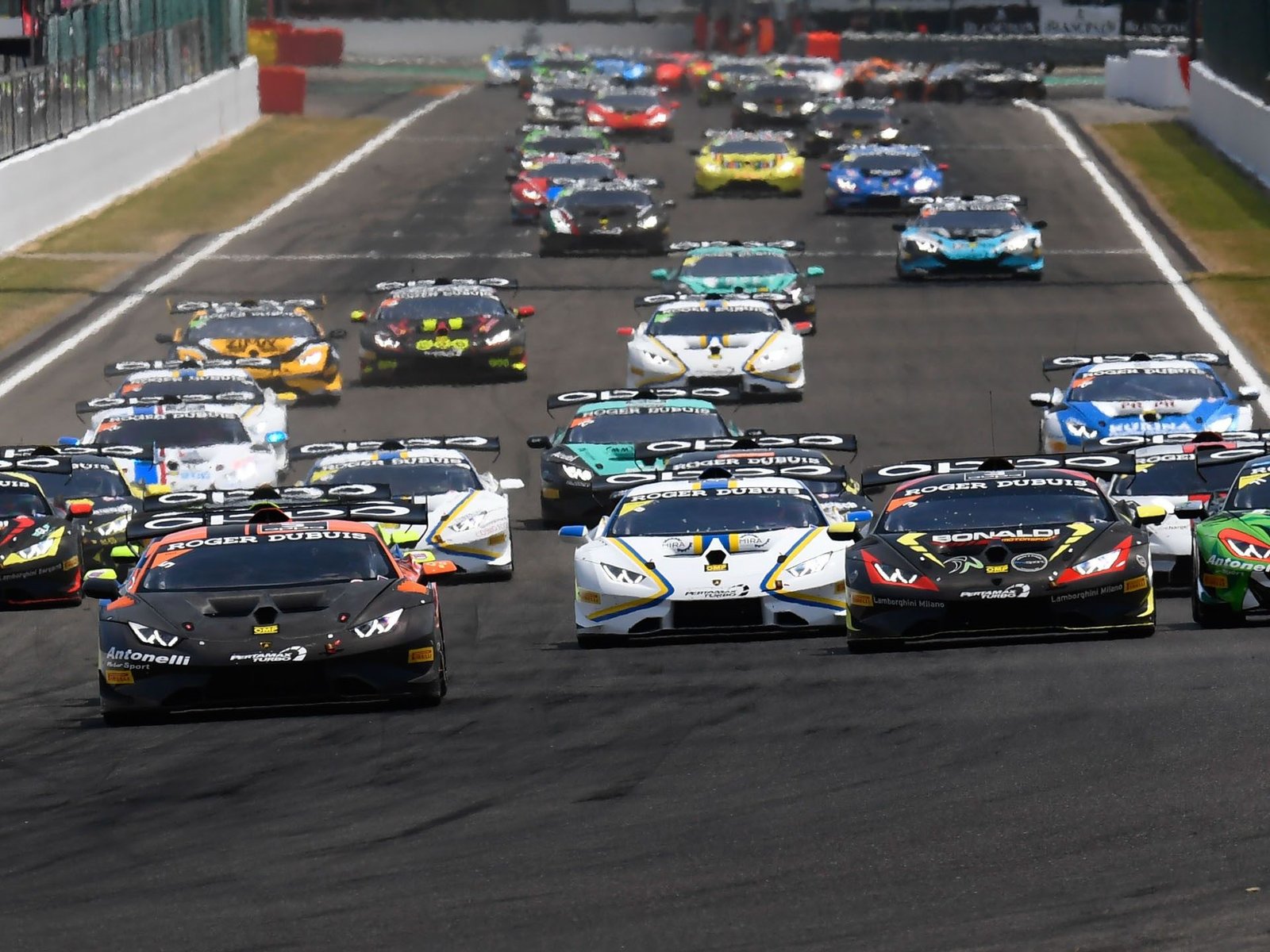 Multiple Lamborghini Huracán Super Trofeo race cars in various liveries competing closely on track during a Super Trofeo race
