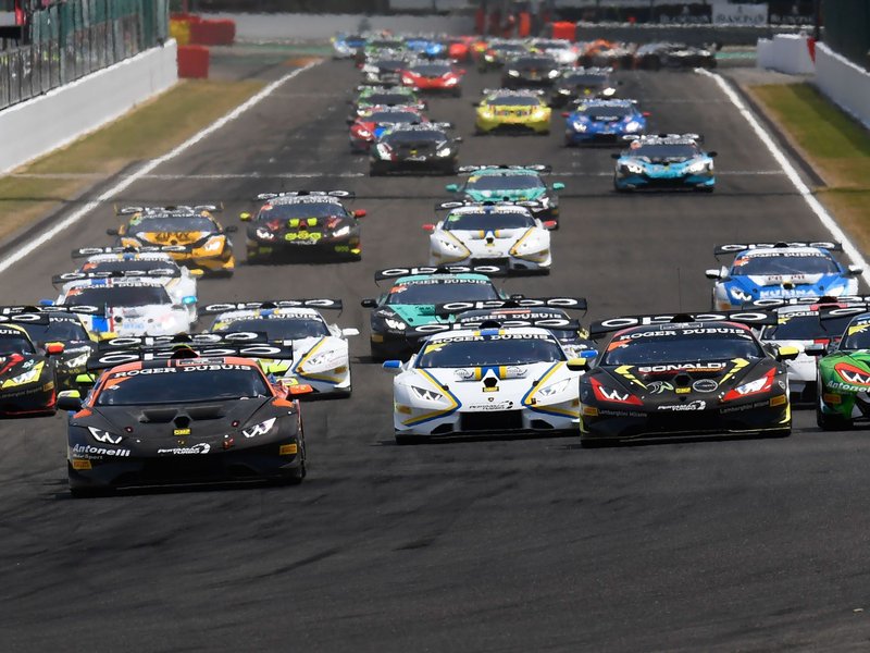 Multiple Lamborghini Huracán Super Trofeo race cars in various liveries competing closely on track during a Super Trofeo race