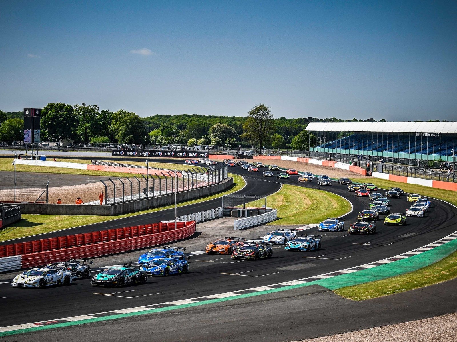 A pack of Lamborghini Huracán Super Trofeo EVO race cars navigating a corner during a Super Trofeo Europe race, with racing liveries, large rear wings, and safety barriers visible