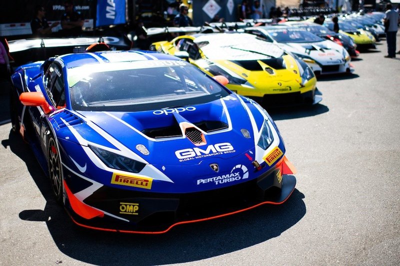 A line of Lamborghini Huracán Super Trofeo race cars with aggressive aero and colorful racing liveries parked in a sunny paddock