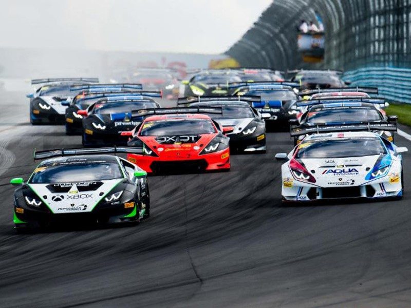 A pack of Lamborghini Huracán Super Trofeo race cars in varied liveries battling for position on track during a North America series race