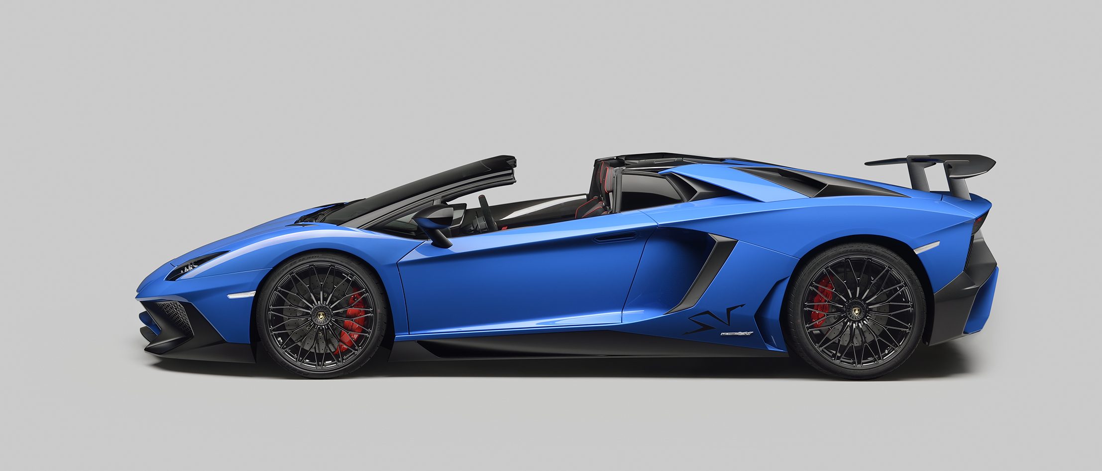 Blue Lamborghini Aventador LP 750-4 Superveloce Roadster side profile in studio showing low stance, large air intakes, and prominent side skirts