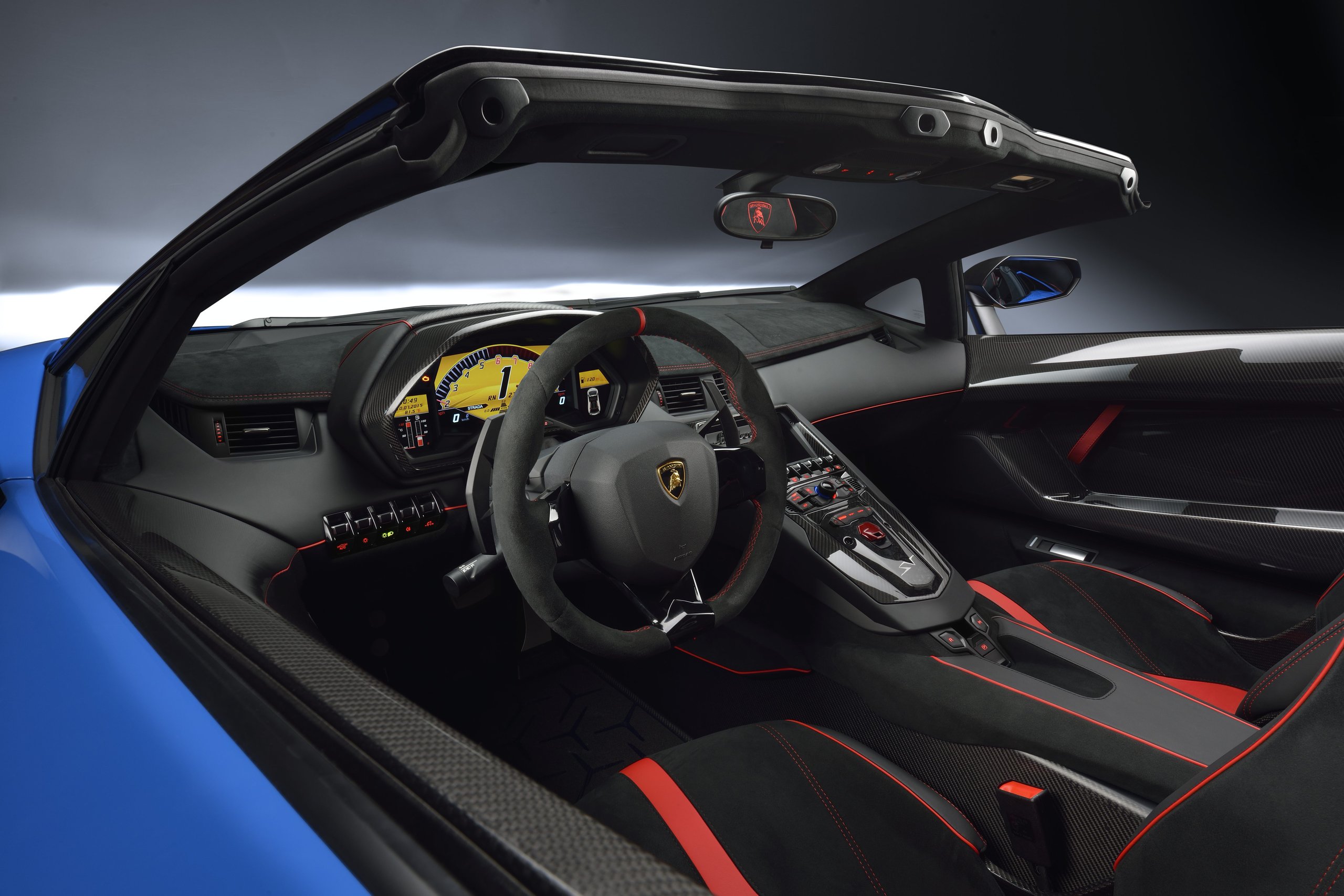 Interior of the Lamborghini Aventador LP 750-4 Superveloce Roadster from the driver's perspective showing carbon fiber trim, sport steering wheel, and digital instrument cluster