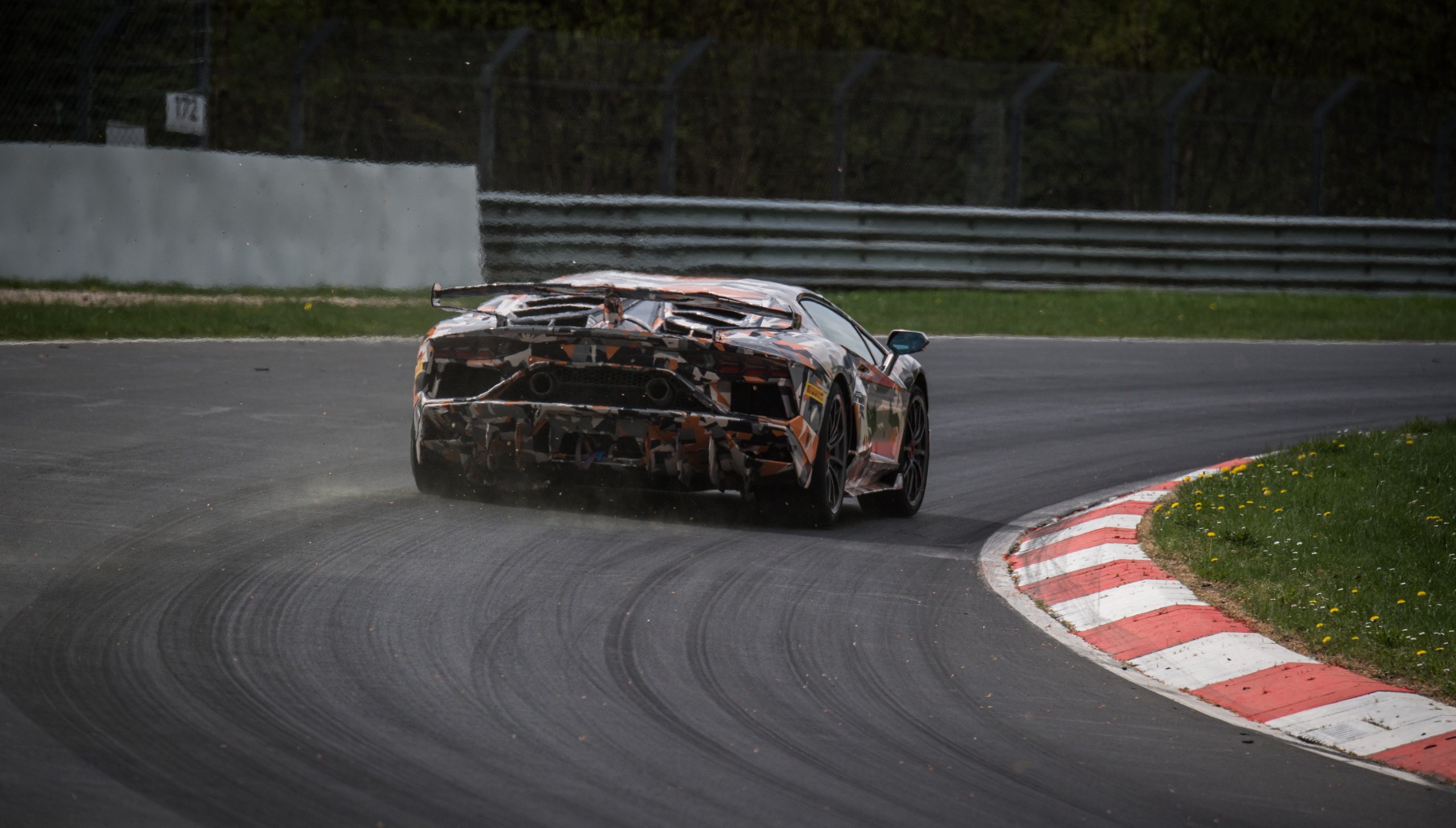 Camouflaged Aventador SVJ speeding away on the Nürburgring, showing large rear wing, aggressive diffuser, and quad exhaust