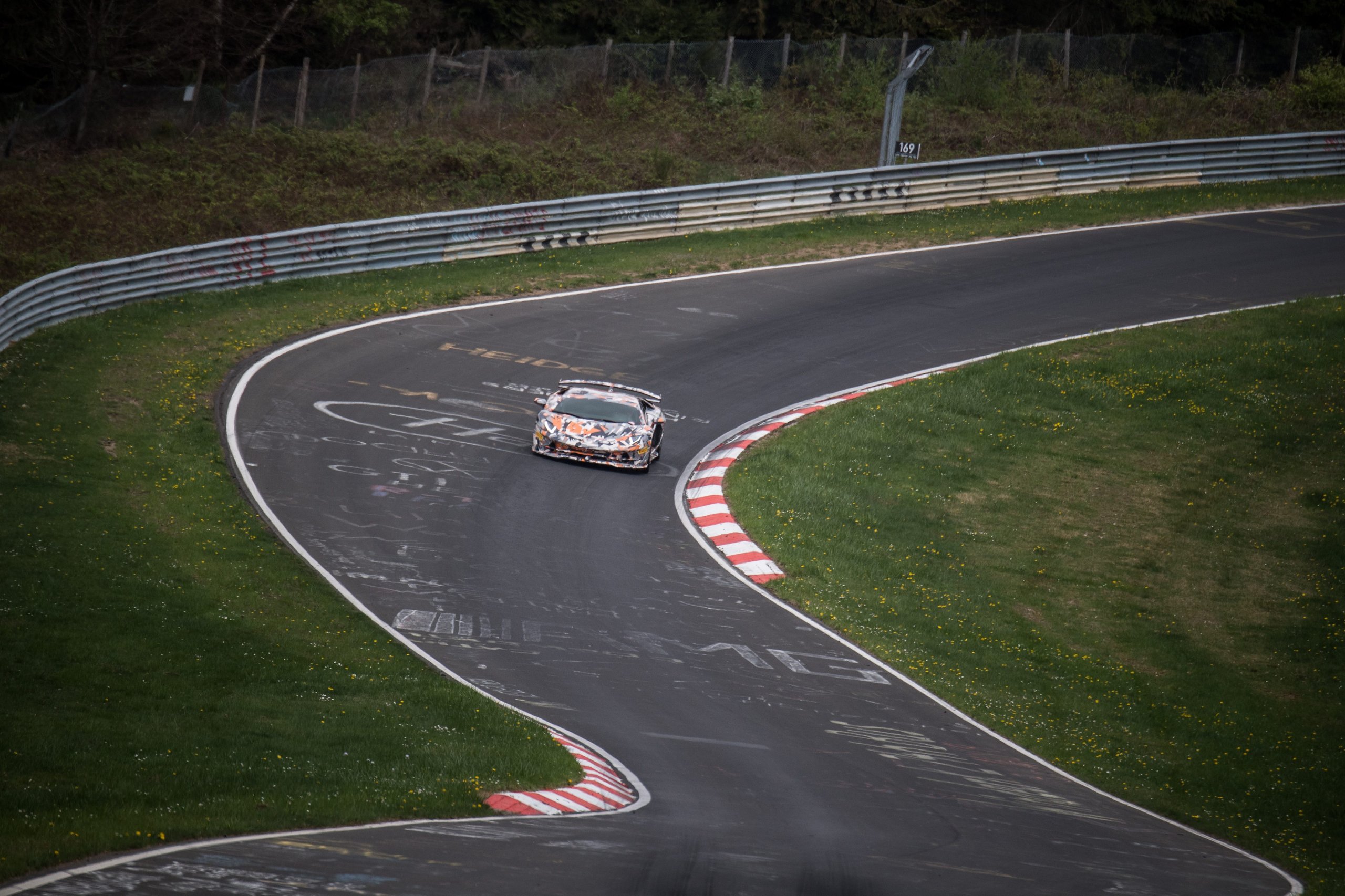 Camouflage-wrapped Aventador SVJ prototype navigating a turn on the Nürburgring, high-angle view showing aggressive aerodynamic elements