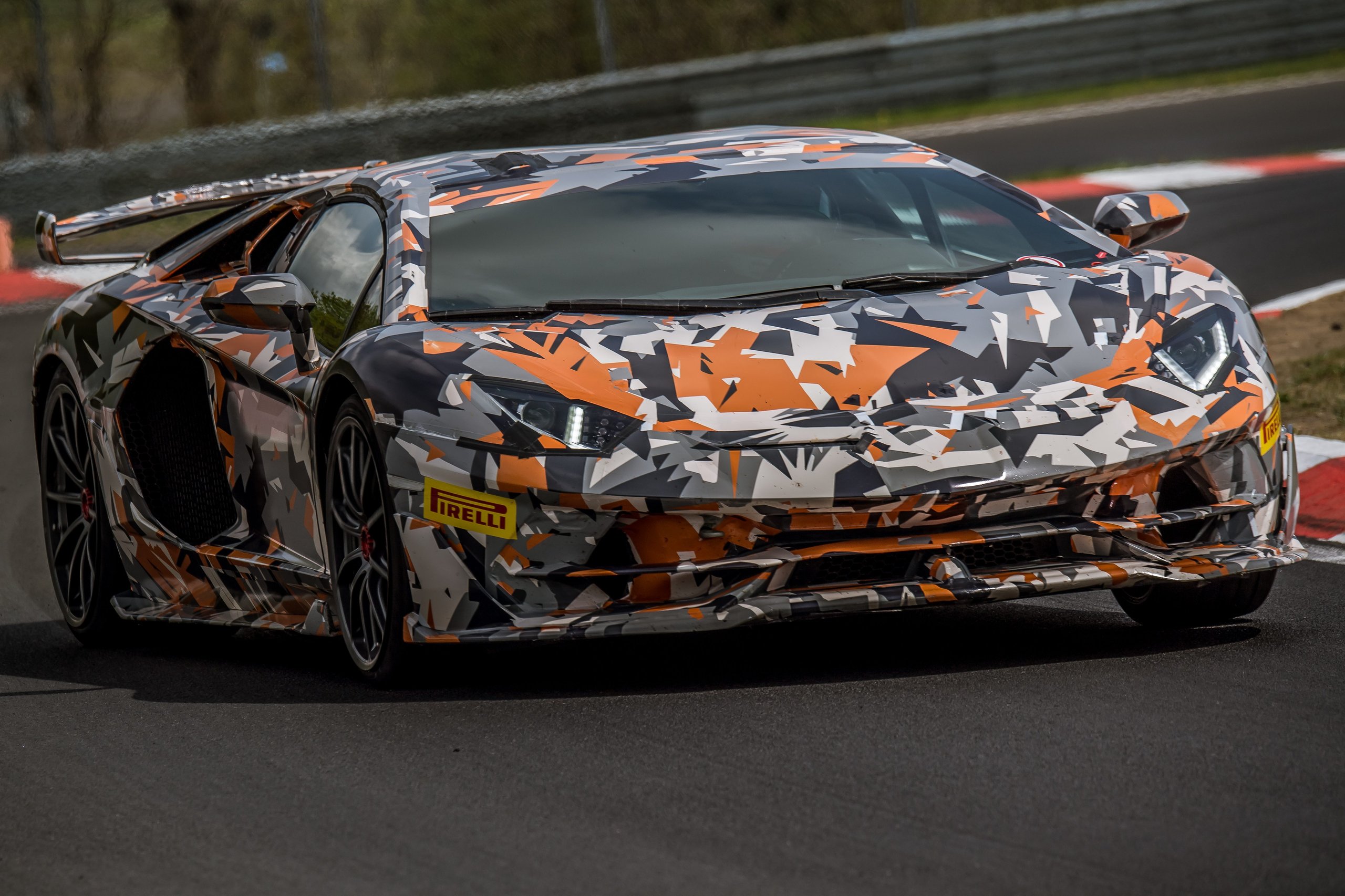 Camouflaged Lamborghini Aventador SVJ prototype at speed on the Nürburgring Nordschleife, low-angle front view showing aggressive air intakes and Pirelli tires