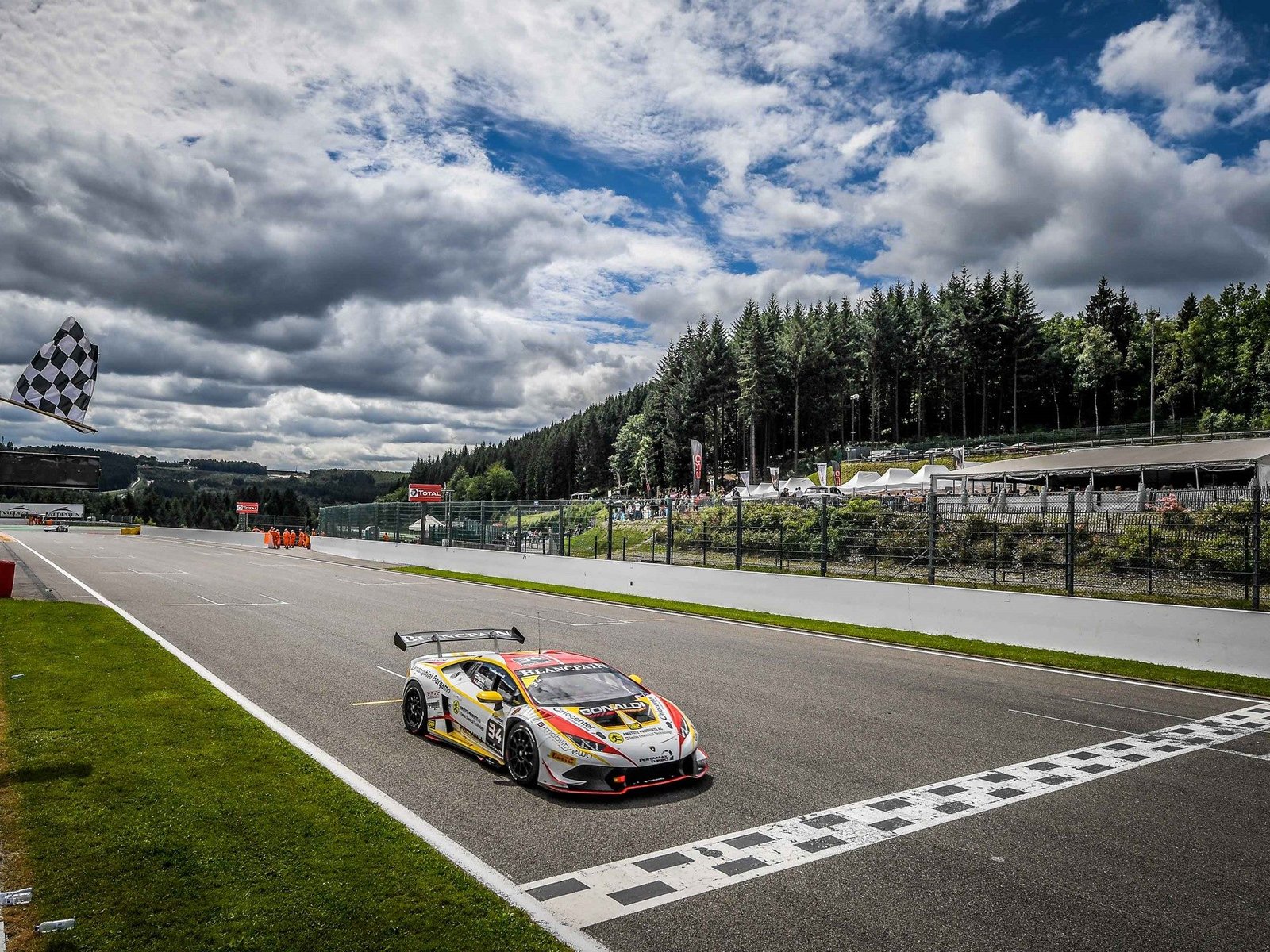 A Lamborghini Huracan Super Trofeo race car crosses the finish line under the checkered flag at Spa-Francorchamps