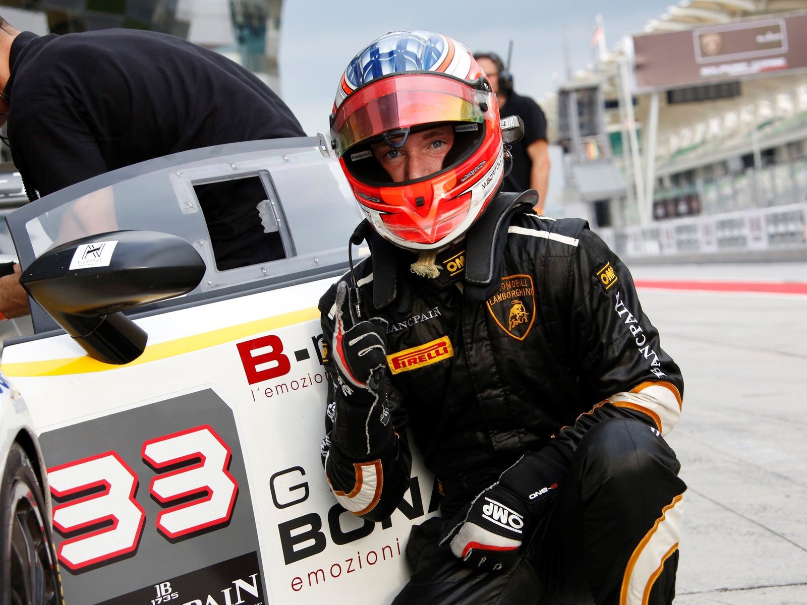 A Bonaldi Motorsport racing driver kneels beside a white Lamborghini Huracan GT3 race car with red number 33 in the pit lane