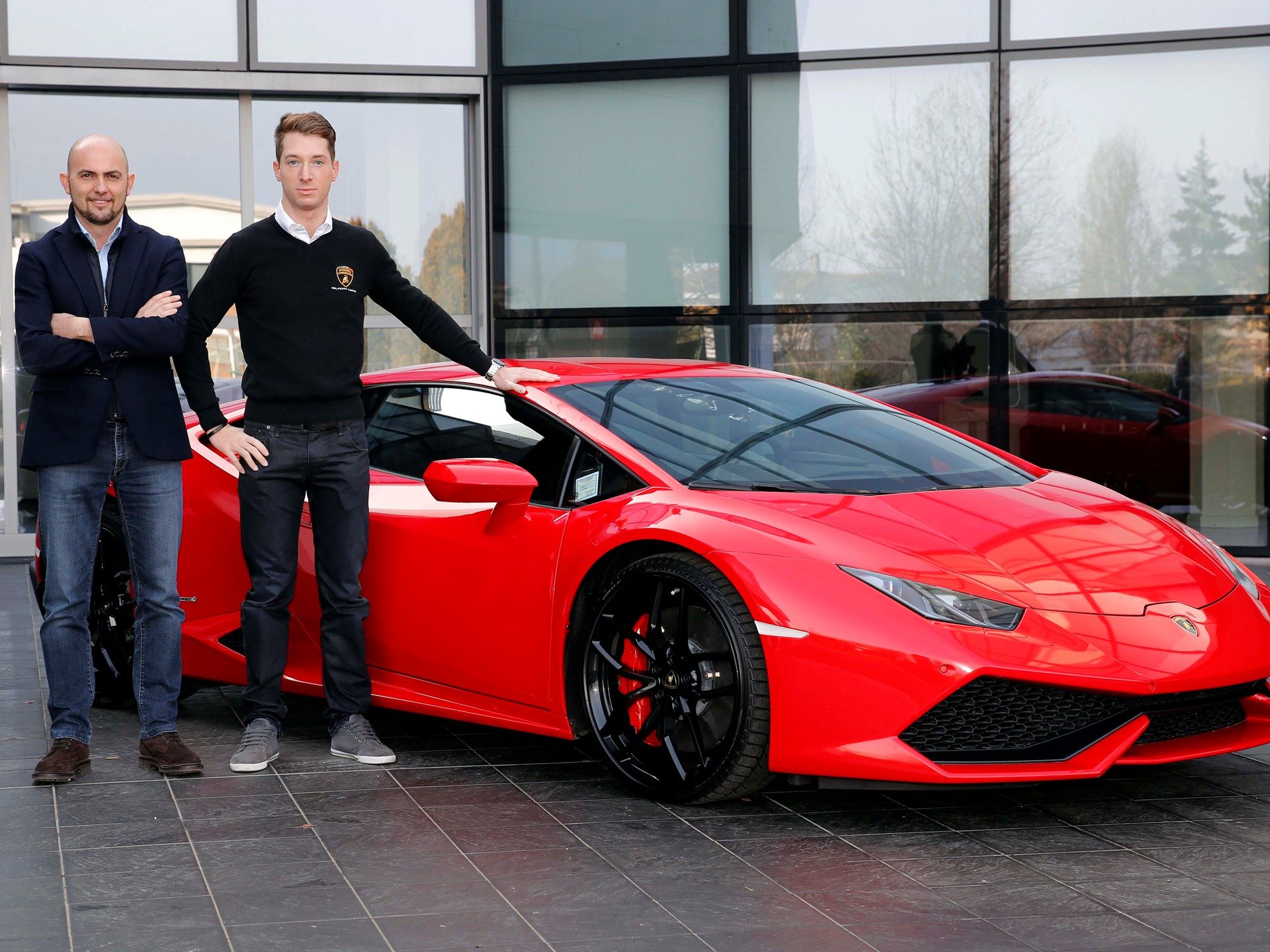 Mirko Bortolotti posing with a red Lamborghini Huracán outside a glass-fronted building