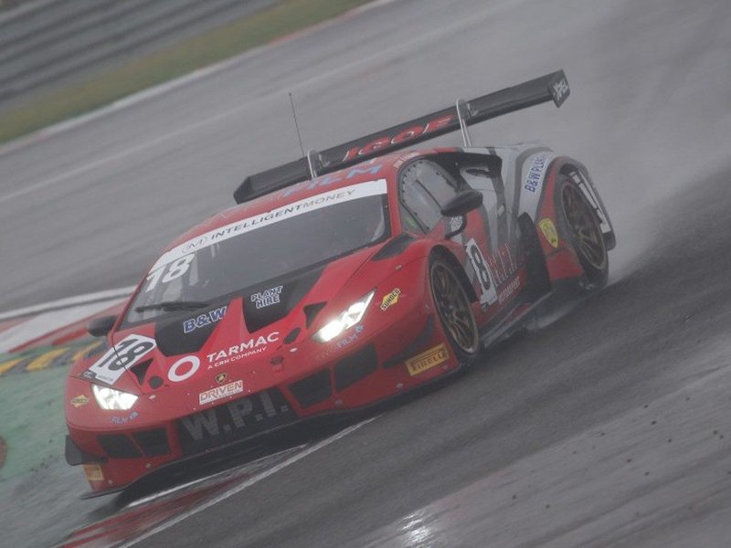Lamborghini Huracán GT3 Evo number 18 cornering on a wet track with tire spray and illuminated headlights visible