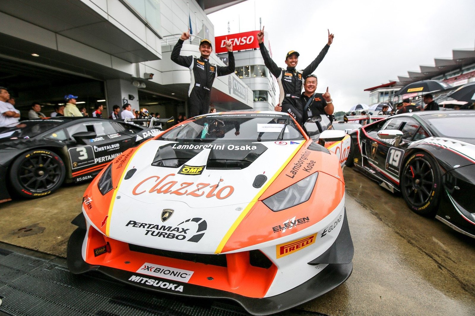 Drivers celebrate atop an orange and white Lamborghini Huracán Super Trofeo race car in the Fuji Speedway pit lane after their double victory