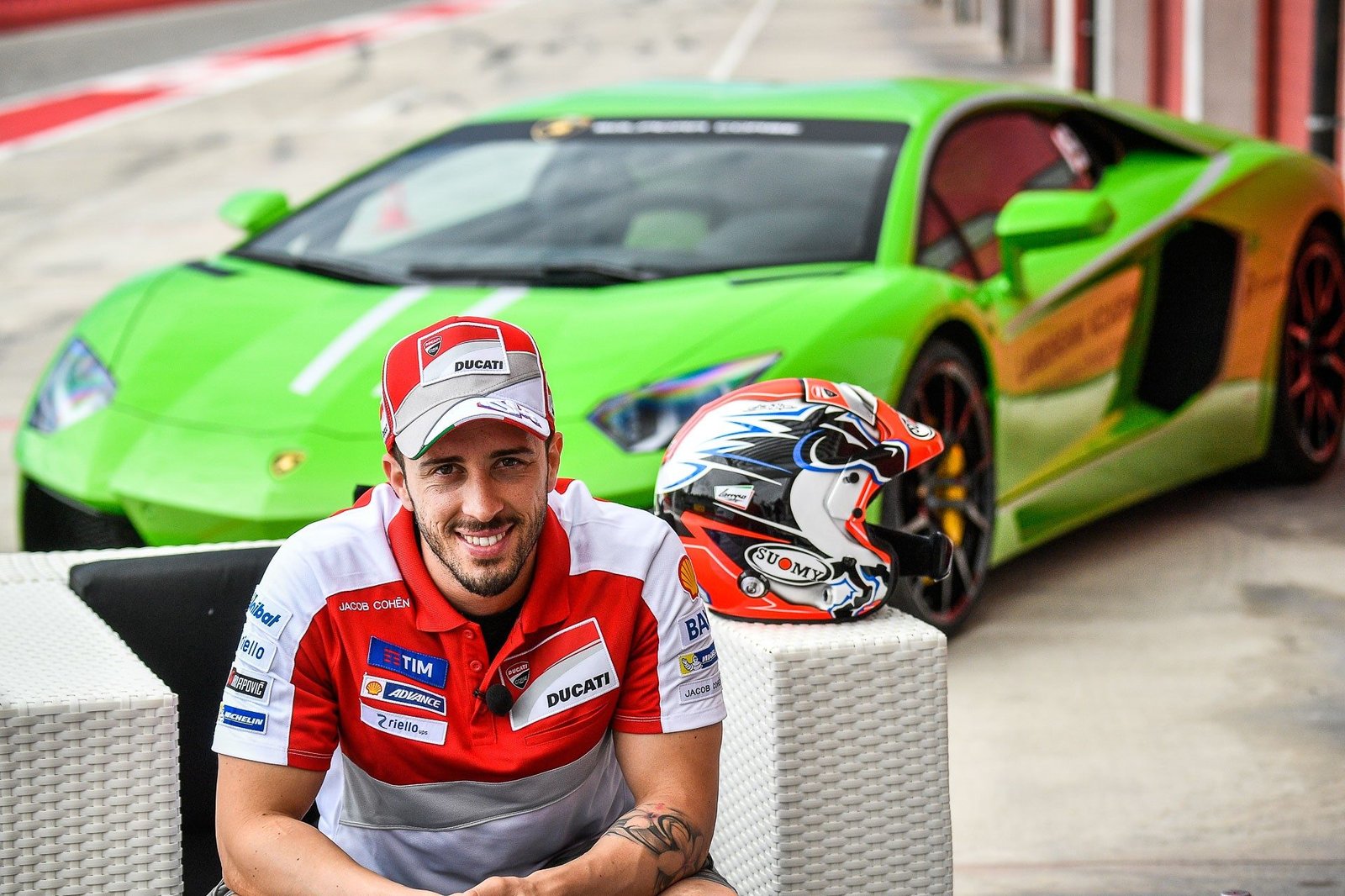 Andrea Dovizioso in racing attire seated in front of a bright green Lamborghini Huracán Super Trofeo on a racetrack