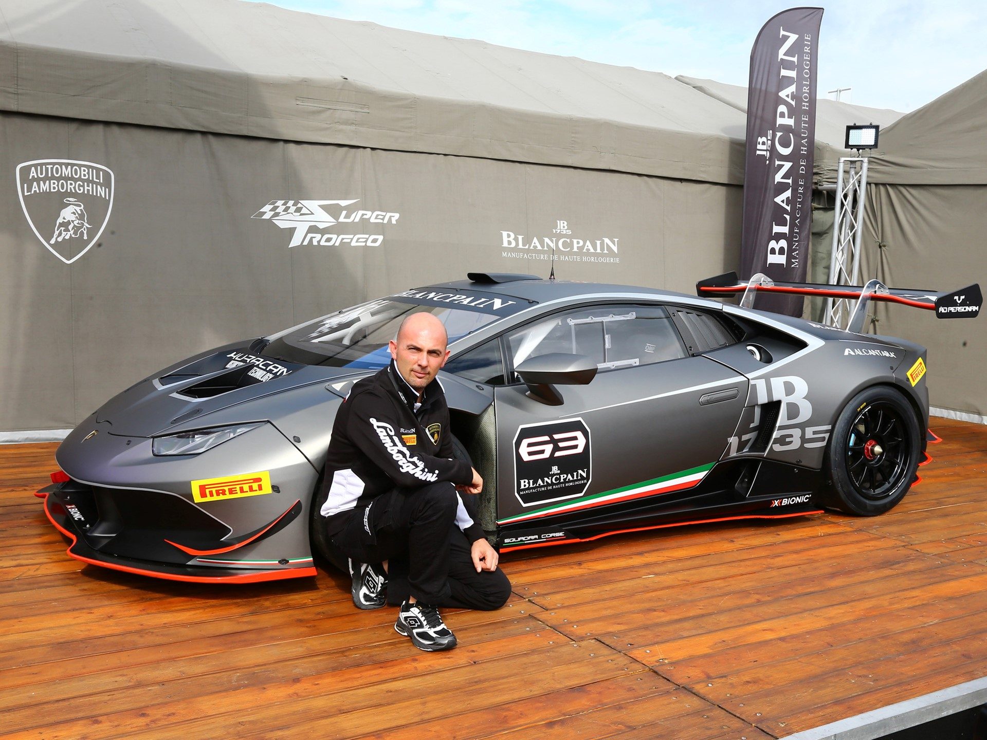 Giorgio Sanna in racing suit beside a Lamborghini Huracán Super Trofeo showing its large rear wing and racing livery