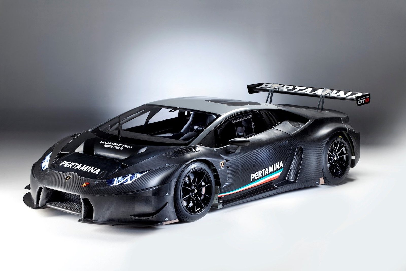 Lamborghini Huracán GT3 in black livery with Pertamina sponsorship, featuring exposed carbon fiber panels, large rear wing, and racing slick tires