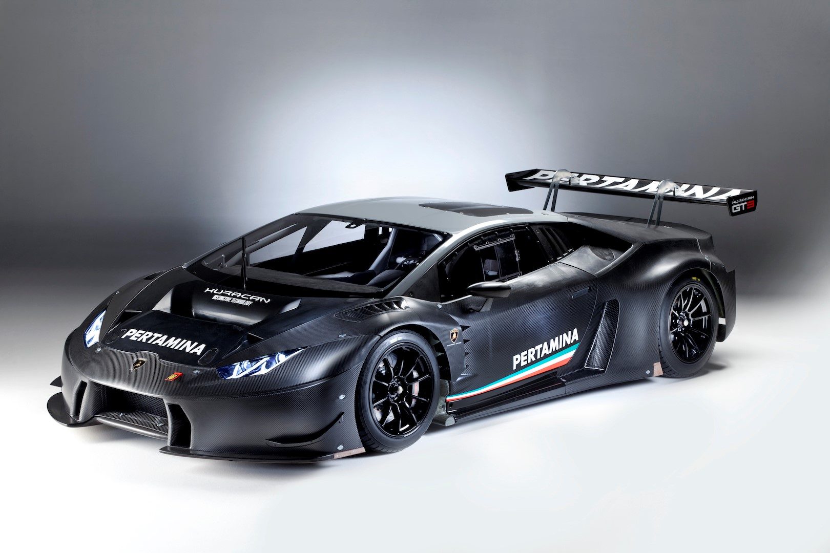 Lamborghini Huracán GT3 in black livery with Pertamina sponsorship, featuring exposed carbon fiber panels, large rear wing, and racing slick tires