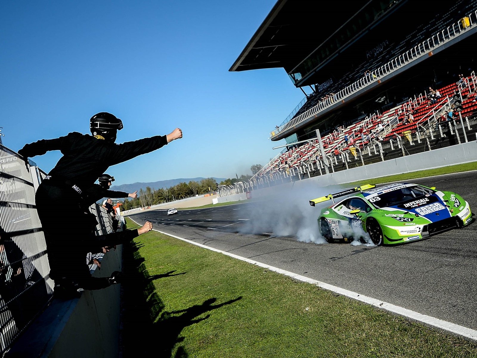 Lamborghini Huracán GT3 in Imperiale Racing livery performing a celebratory burnout while a team member pumps his fist from behind the barrier