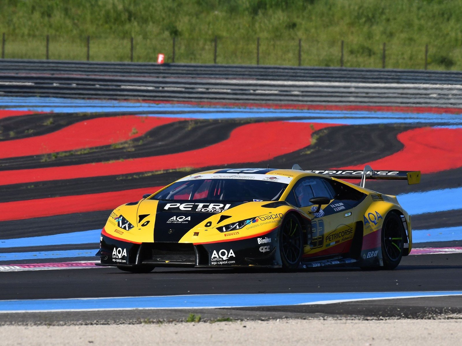 Yellow and black Lamborghini Huracán GT3 race car at speed on a circuit with red and blue track markings