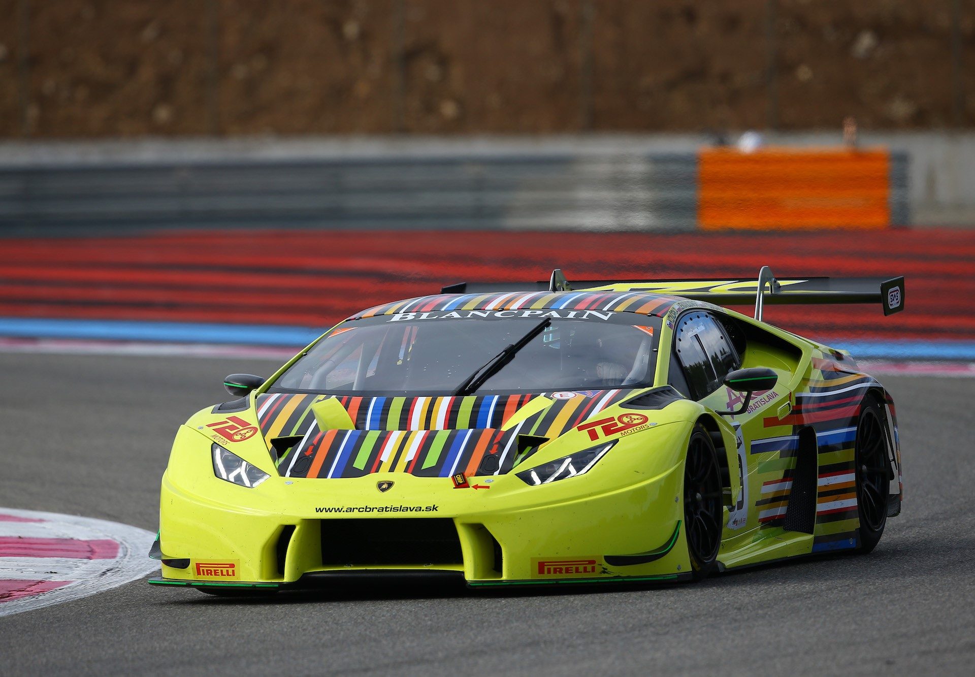 Yellow Lamborghini Huracán GT3 race car with multi-colored striped livery at speed on a racetrack during the 2016 Blancpain GT Series test days