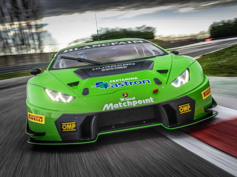 Green Lamborghini Huracán GT3 race car at speed on track with dramatic sky, showing aggressive aero kit and racing livery