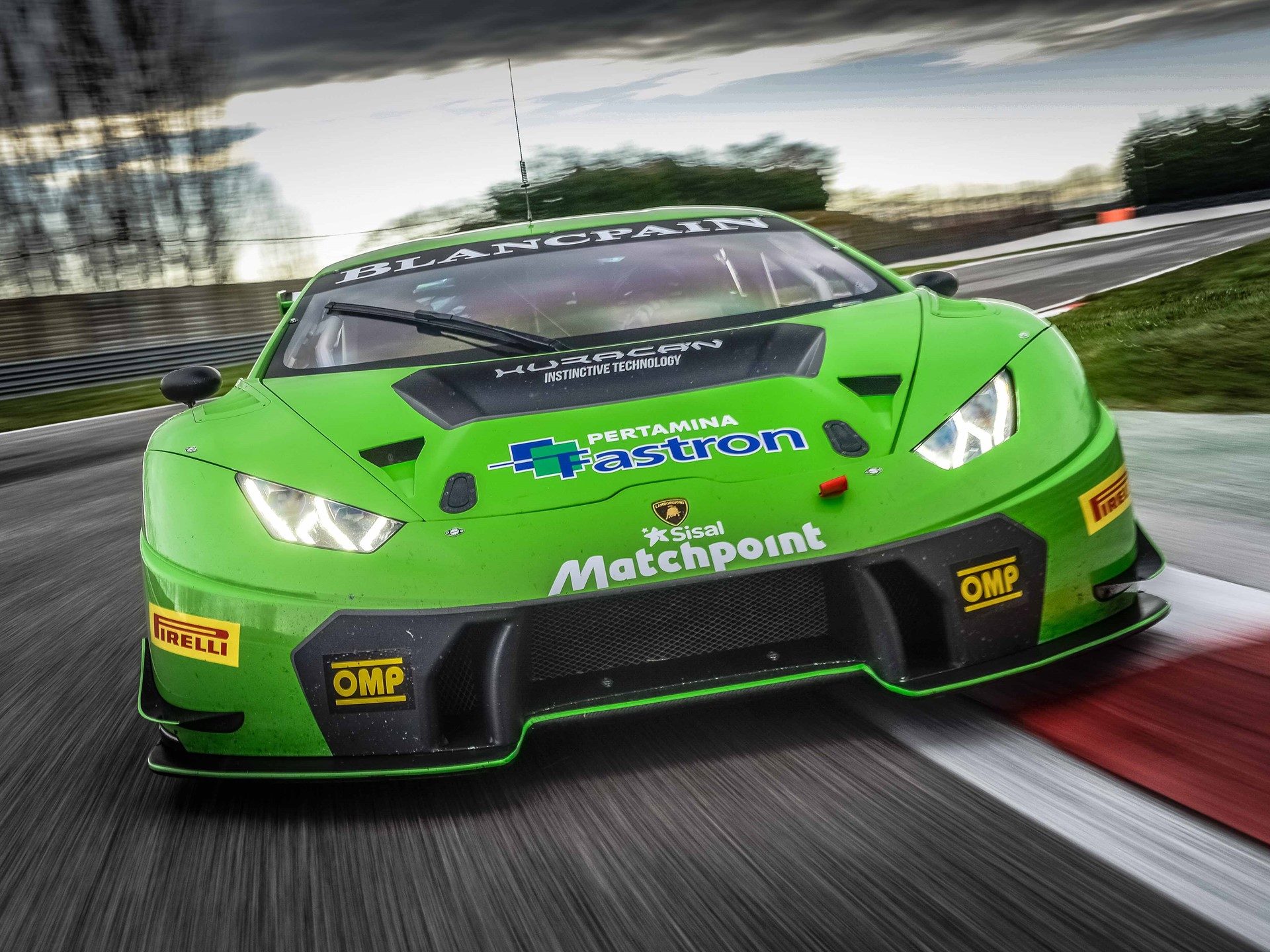 Green Lamborghini Huracán GT3 race car at speed on track with dramatic sky, showing aggressive aero kit and racing livery