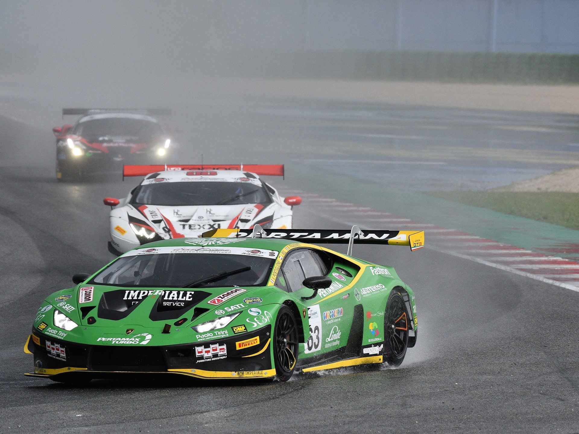 Green Lamborghini Huracán GT3 EVO leads competitors on a wet race track during a GT championship event