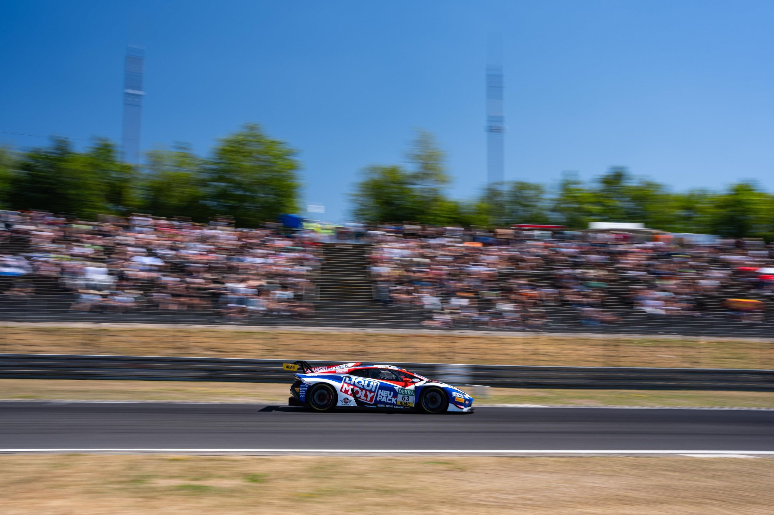The #63 lamborghini huracán gt3 evo2 at speed on the nürburgring with blurred spectators in the background