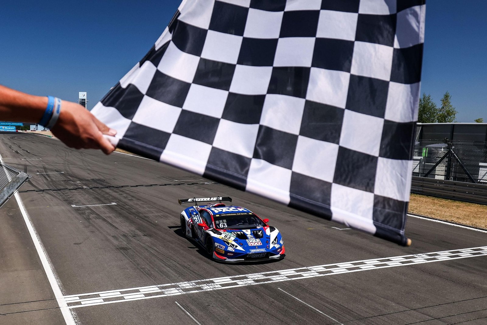 The #63 Lamborghini Huracán GT3 EVO2 crosses the finish line under the checkered flag at the Nürburgring ADAC GT Masters
