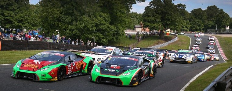 Two lamborghini huracán gt3 race cars leading a pack of gt competitors on a racetrack with spectators in the background