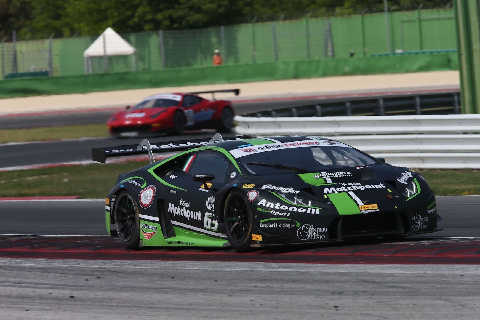 Black and green Lamborghini Huracán GT3 race car on track at Misano with a red competitor visible in the background