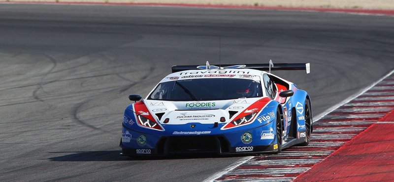 Blue, white, and red Lamborghini Huracán GT3 race car at speed on the Misano World Circuit, showcasing its large rear wing and racing livery