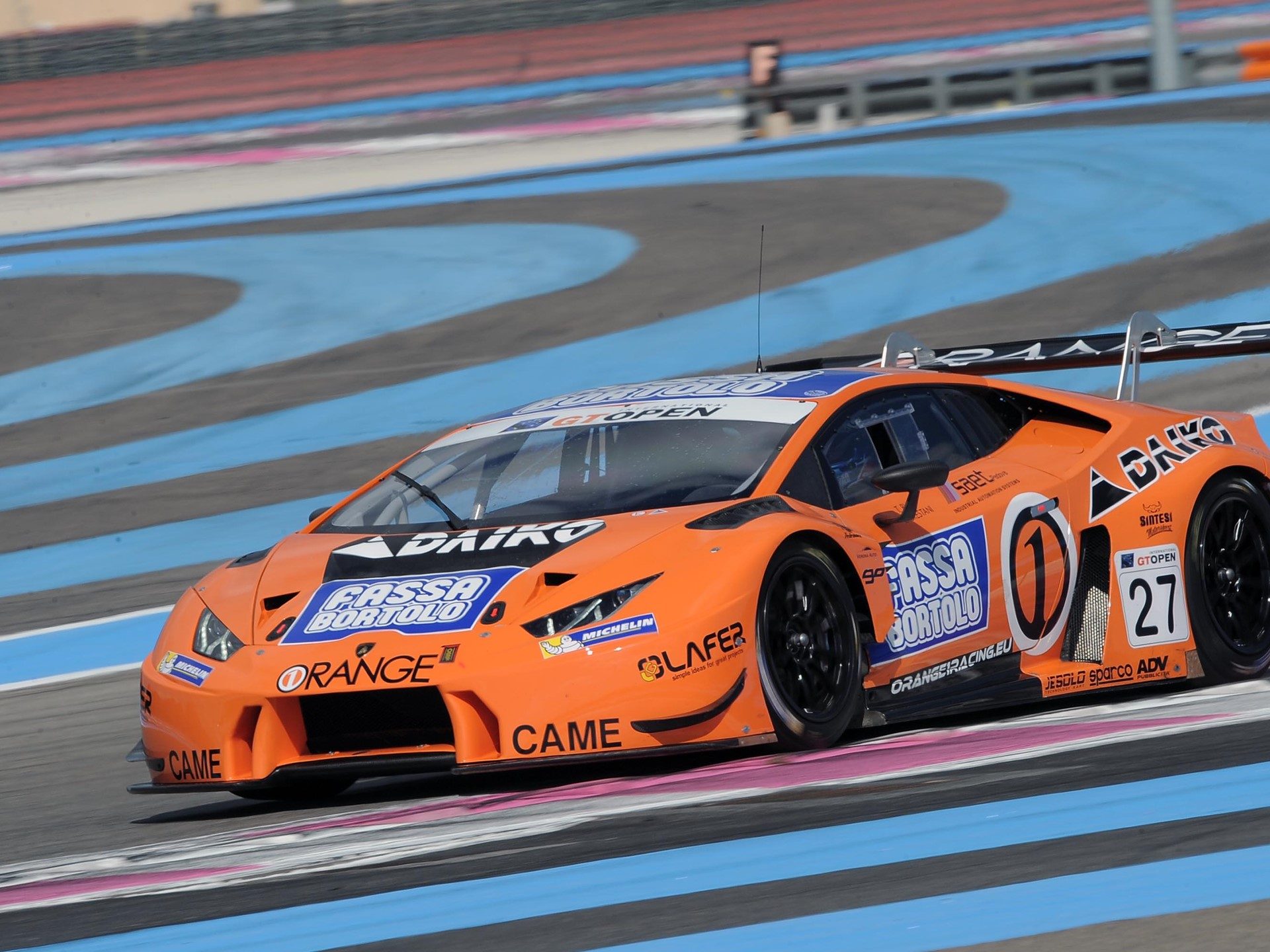 Orange Lamborghini Huracán GT3 race car at speed on a racetrack with visible aerodynamic kit and large rear wing