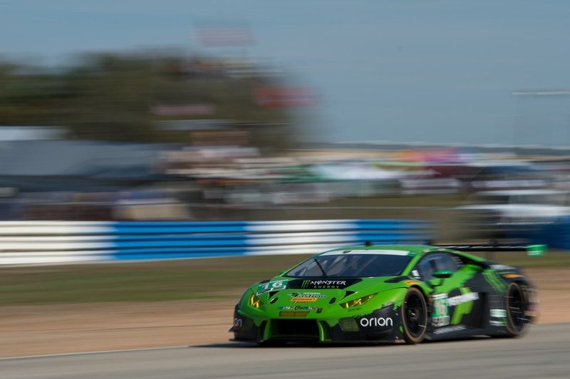Green Lamborghini Huracán GT3 race car at speed on track with motion blur