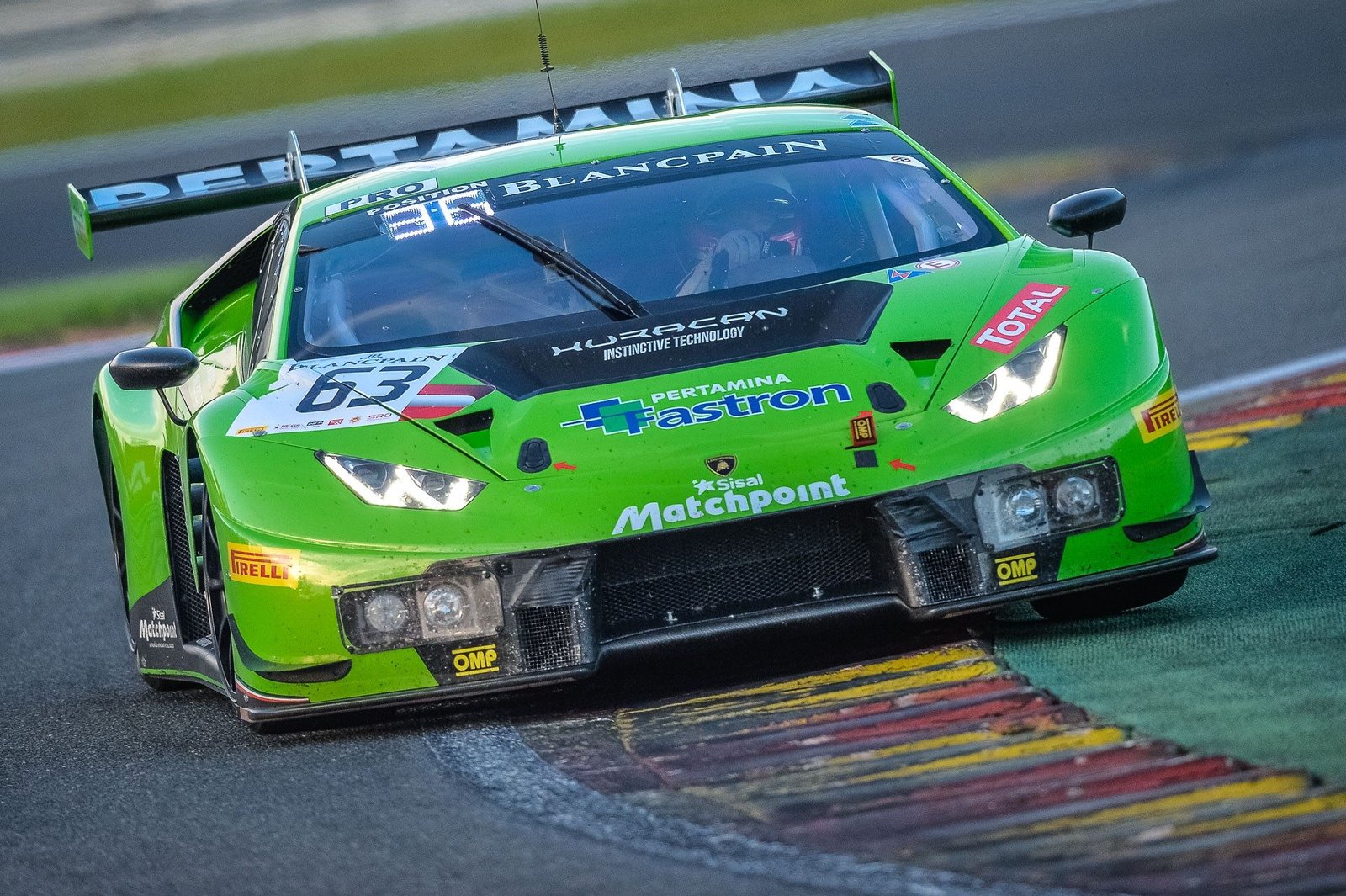 Vibrant green Lamborghini Huracan GT3 race car with sponsor livery navigating a turn at Spa with headlights illuminated