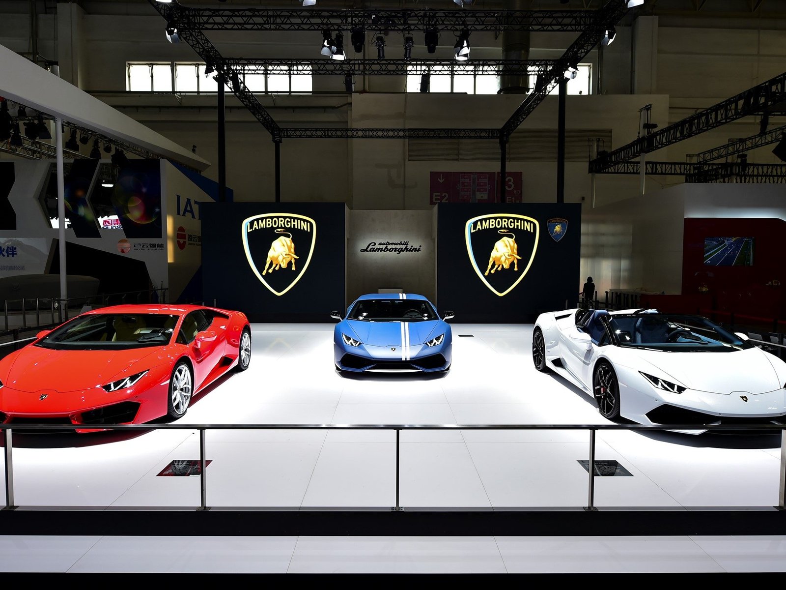 Three Lamborghini Huracán models in red, blue, and white displayed on stage at the 2016 Beijing International Motorshow