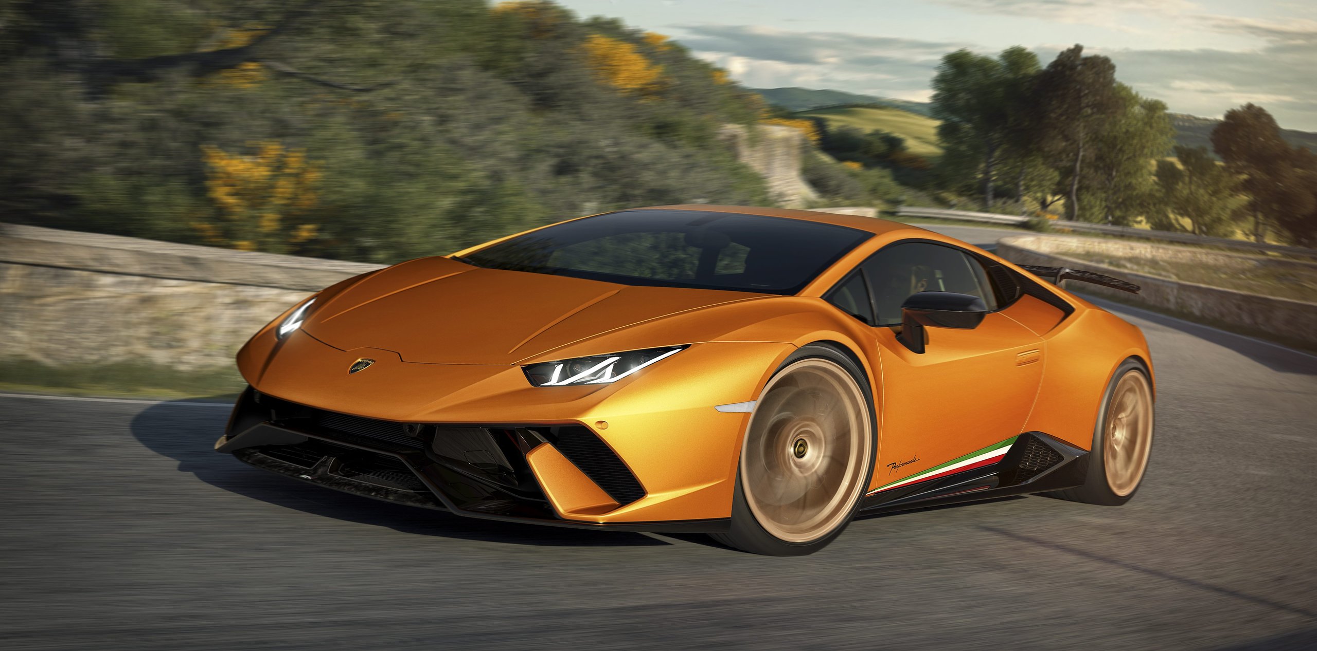 How The Huracán Performante Used Invisible Aerodynamics To Beat A 887-Hp Hybrid Around The Nürburgring 7 Orange huracán performante at speed on a winding road, low front three-quarter angle showing the aggressive front fascia and lightweight forged wheels